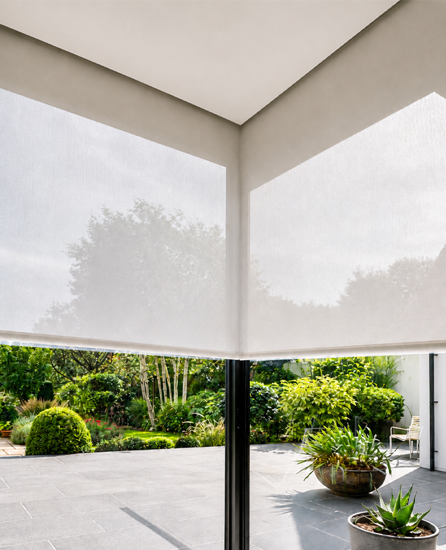 Decorquip white roller blinds in Blindspace partially lowered over corner windows overlooking a garden