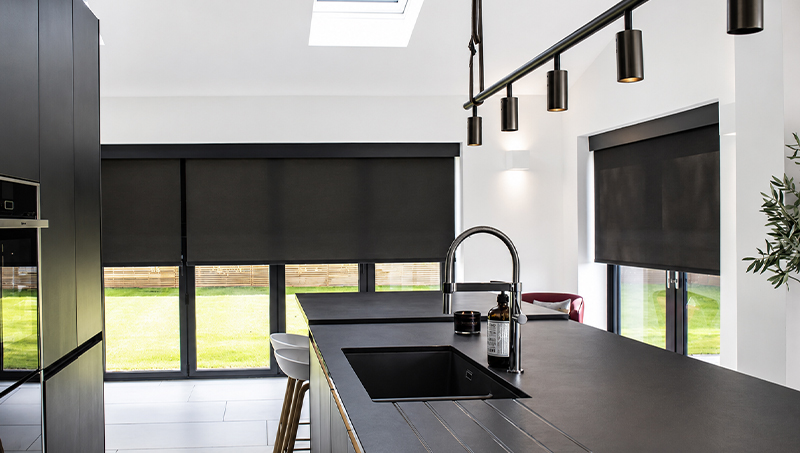 Decorquip black roller blinds partially lowered in a modern kitchen with large windows