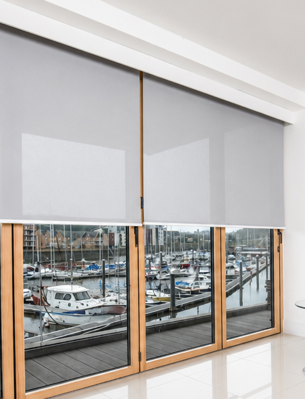 Decorquip grey roller blinds with white Capital Fascia partially lowered across large timber-framed windows overlooking a marina in a modern interior