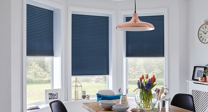 Decorquip dark blue free-hanging pleated blinds partially lowered across dining room bay windows