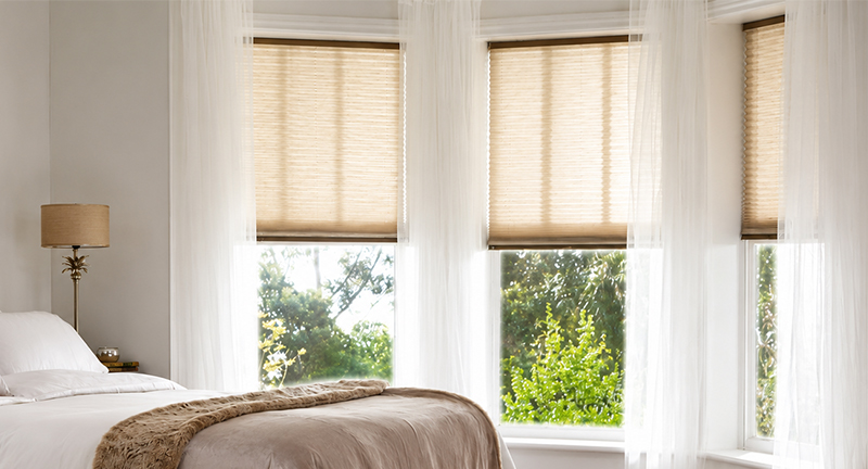 Decorquip beige free-hanging pleated blinds partially lowered in a bright bedroom